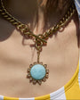 Person wearing a gold chain necklace with a blue pendant, wearing a striped shirt and yellow top.