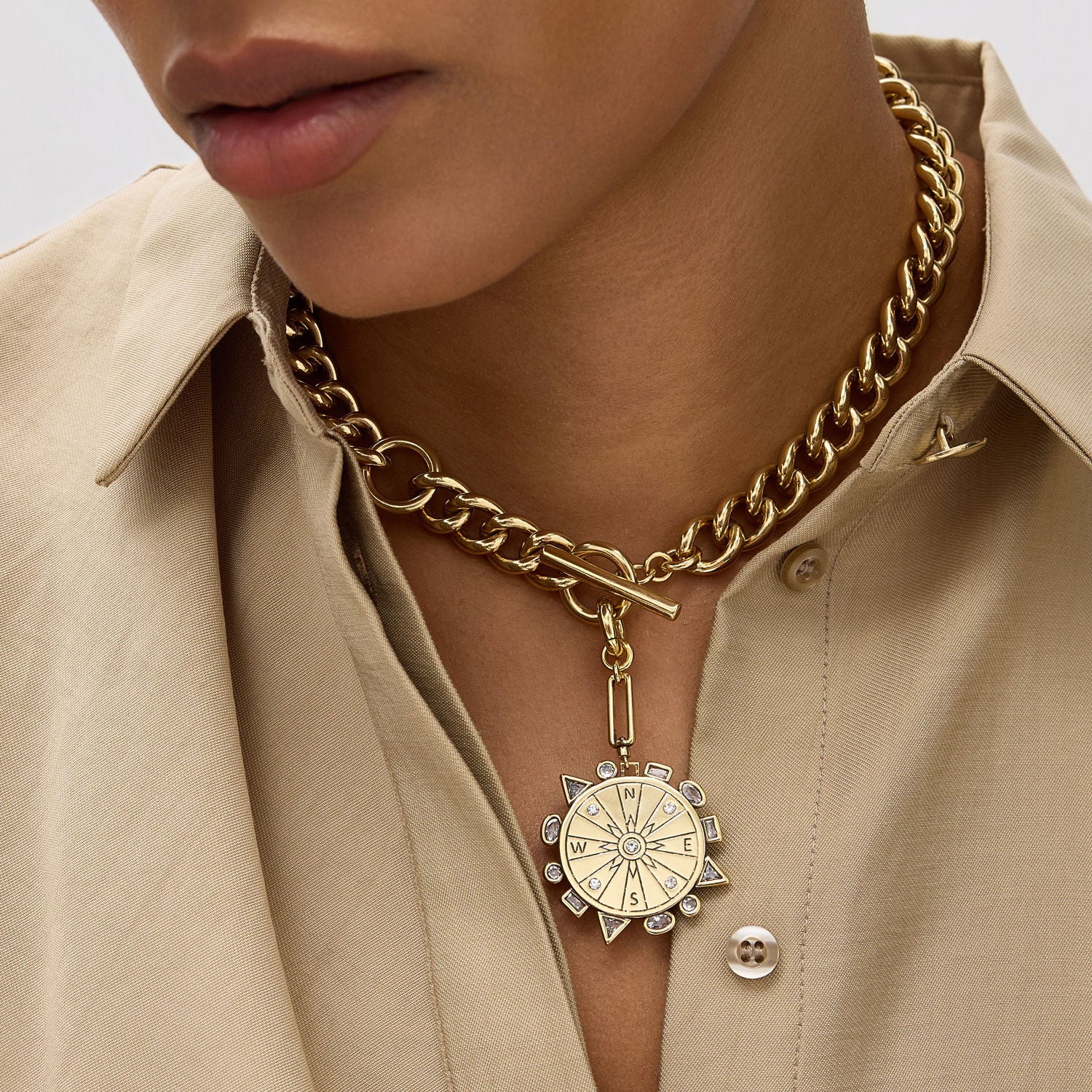 Model wearing a thick gold link chain necklace with a gold compass pendant.