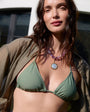 Woman wearing a light purple beaded necklace and mother of pearl charm with green bikini and brown cardigan outdoors