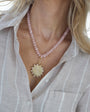 Necklace with pink beads and a gold pendant worn by a person in a light gray shirt.