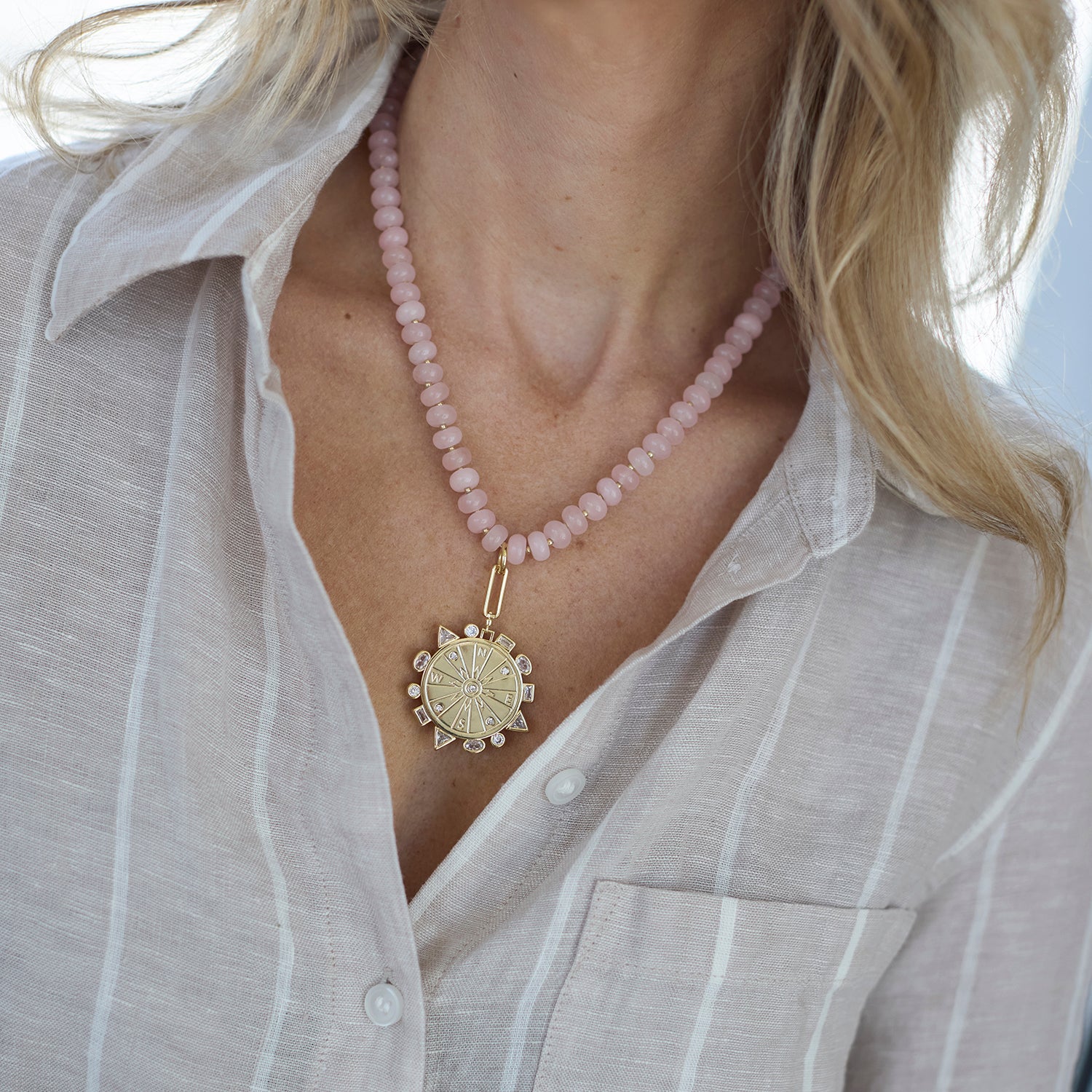 Necklace with pink beads and a gold pendant worn by a person in a light gray shirt.