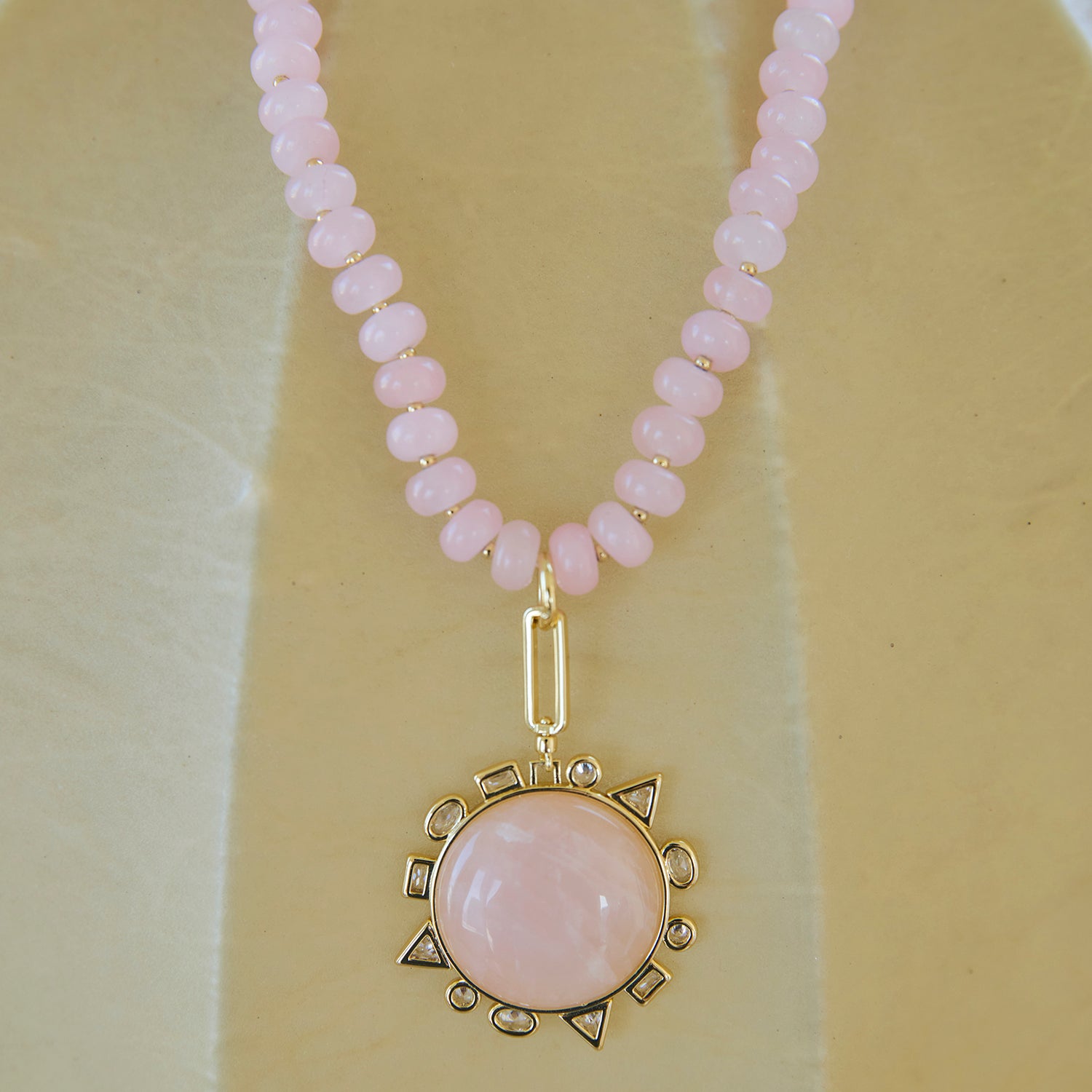 Necklace with pink beads and a gold pendant on a beige background