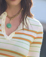 Woman wearing a striped shirt and gold necklace with a green pendant, blurred background