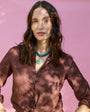 Woman wearing a brown blouse, chunky green necklace with charm against a green background
