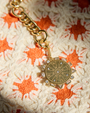 Gold pendant with crystals and compass etching against orange and white crochet background