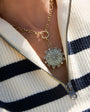 Gold compass pendant necklace on a person wearing a striped sweater