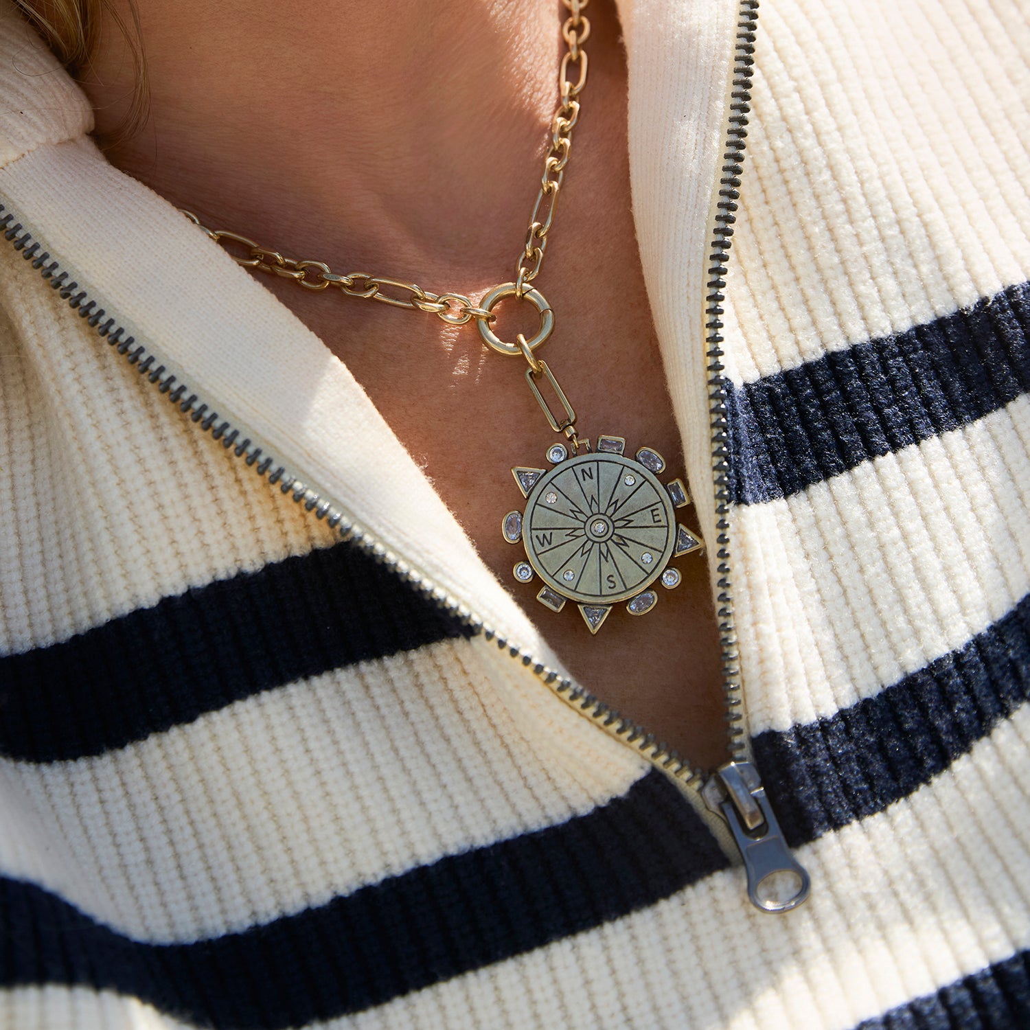 Gold compass pendant necklace on a person wearing a striped sweater
