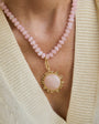 Necklace with pink beads and a gold pendant worn by a person in a beige sweater.