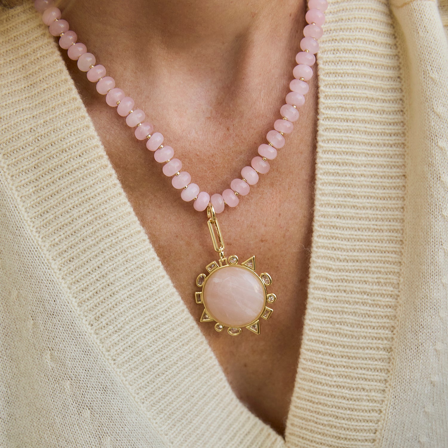 Necklace with pink beads and a gold pendant worn by a person in a beige sweater.