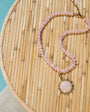 Necklace with pink beads and a large pink stone pendant on a woven surface.