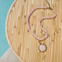 Necklace with pink beads and a large pink stone pendant on a woven surface.