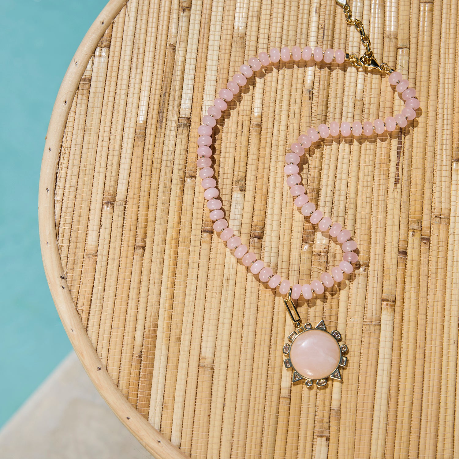 Necklace with pink beads and a large pink stone pendant on a woven surface.