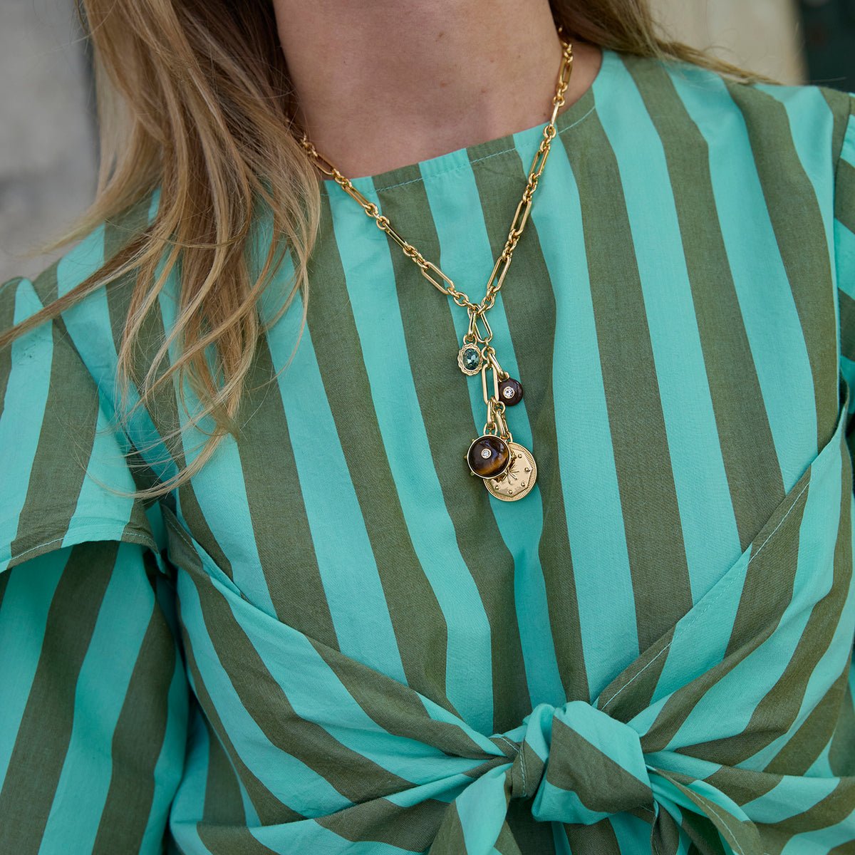 Model wearing  charm and chain necklace with a striped shirt