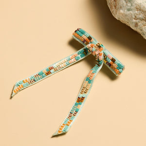 Orange Tan Turquoise and Brown Sequin Hairbow Staged on Flat Cream Background with a Rock
