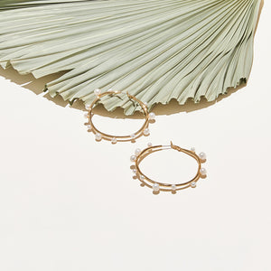 Organic Shaped Gold and Pearl Hoop Earrings Staged with Palm Leaf On Cream Background