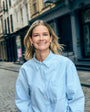 Woman in a light blue striped shirt and gold and pearl hoop earrings standing on a city street.