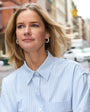 Woman wearing a light blue striped shirt and gold and pearl hoop earrings on a city street