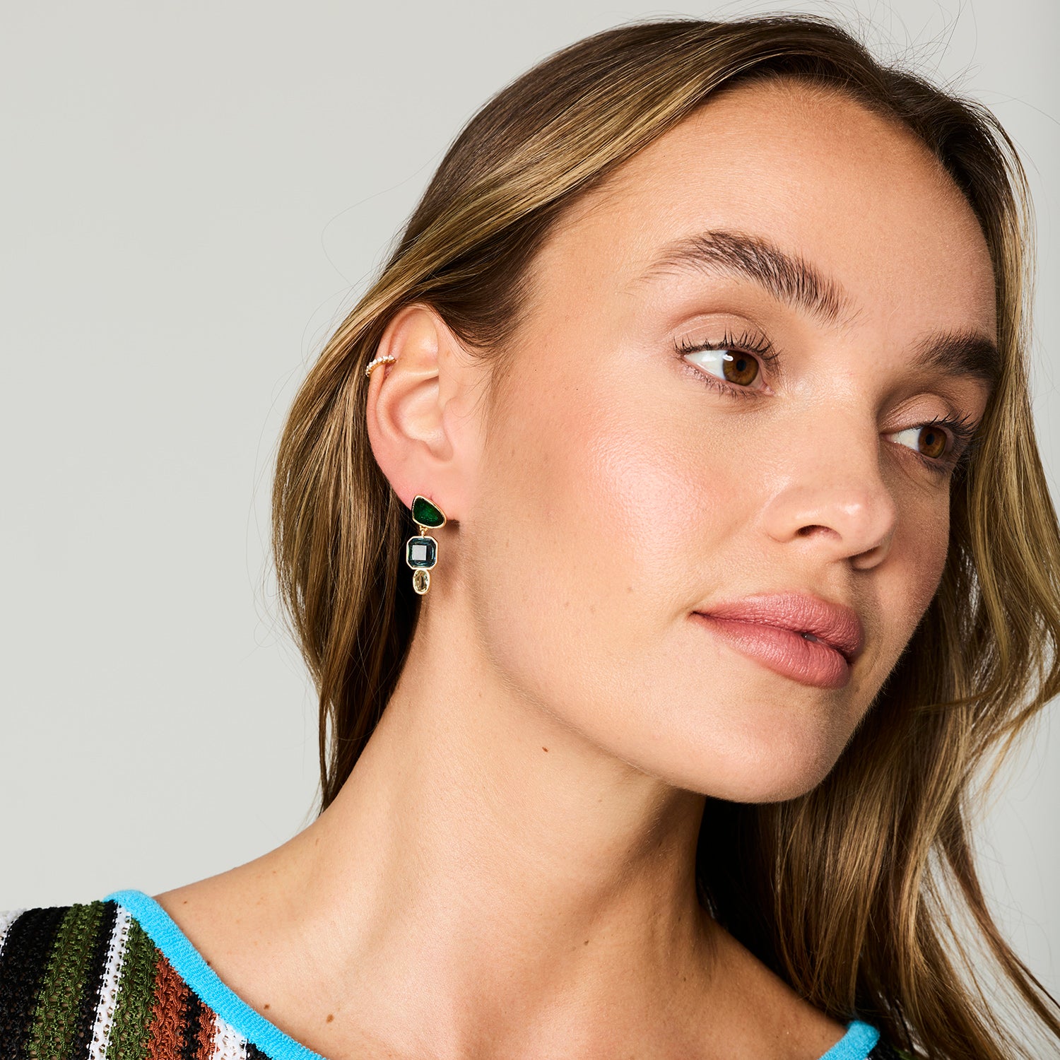 Gold-tone drop earrings featuring faceted green, blue, and clear rectangular stones in a geometric design on Model