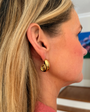Close-up of a woman wearing gold spiral earrings with a blurred indoor background.