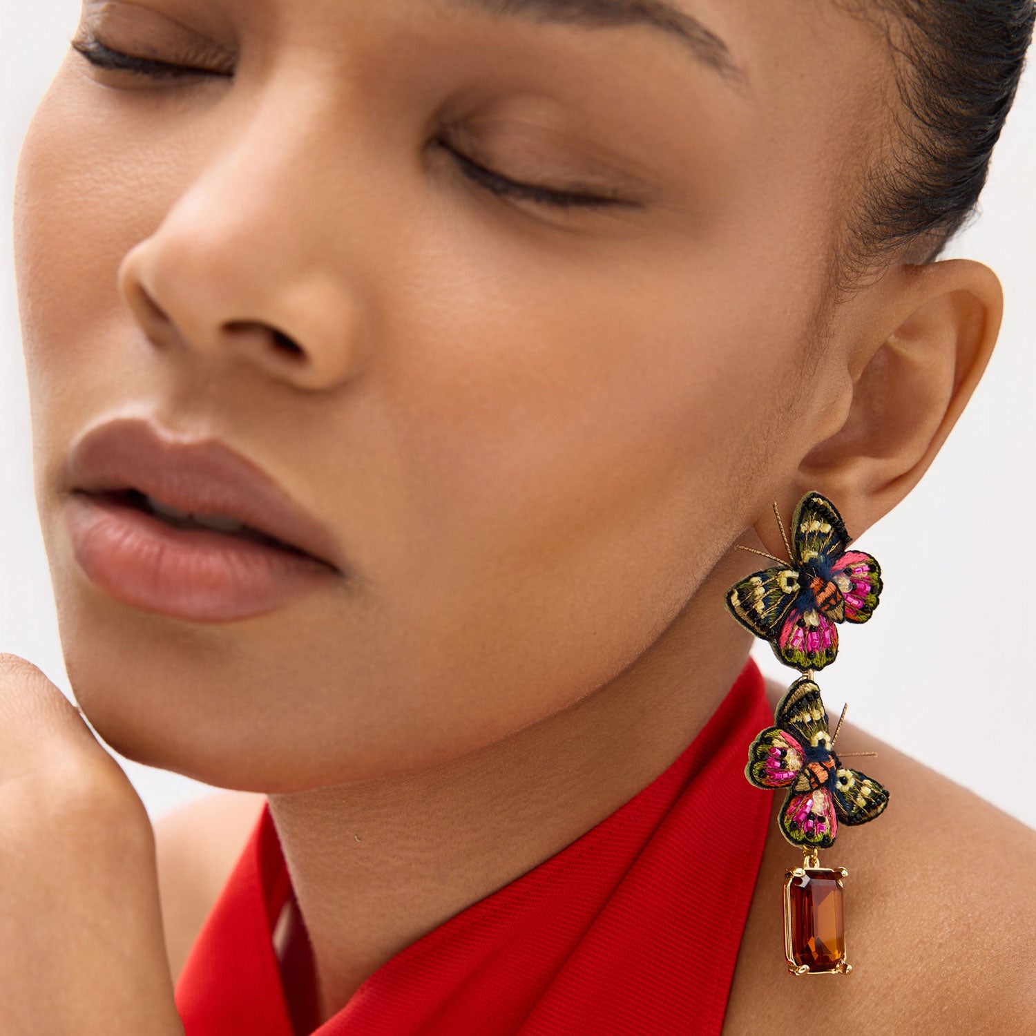 Close-up of a woman wearing a colorful butterfly earring with a red top.