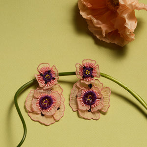 Embroidered and Beaded Pink and Purple Double Drop Flower Earrings Staged on Plant Stem with Flower on Green Background