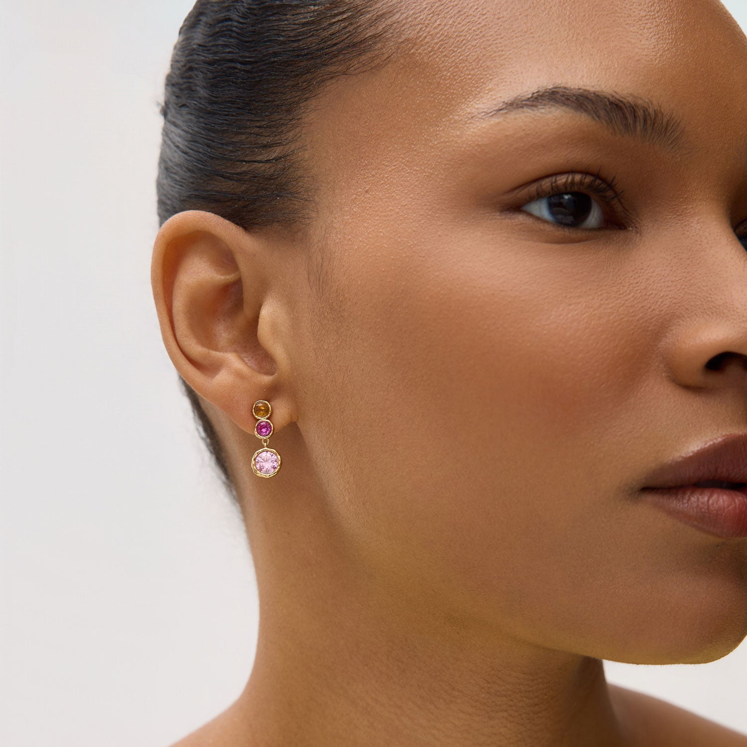 Gold earrings with pink and yellow gemstones on model with neutral background