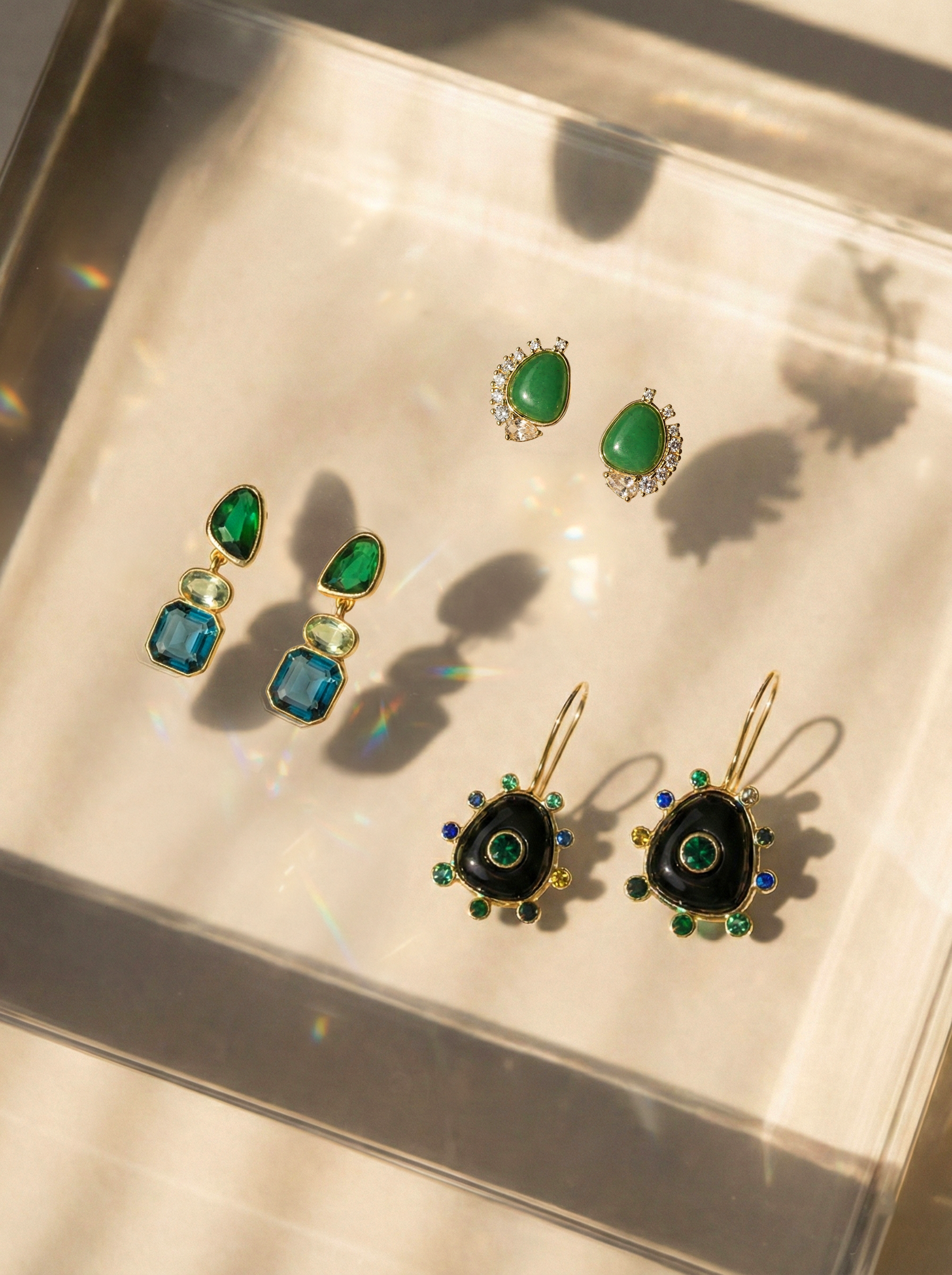 Three sets of statement earrings on a glass reflective background