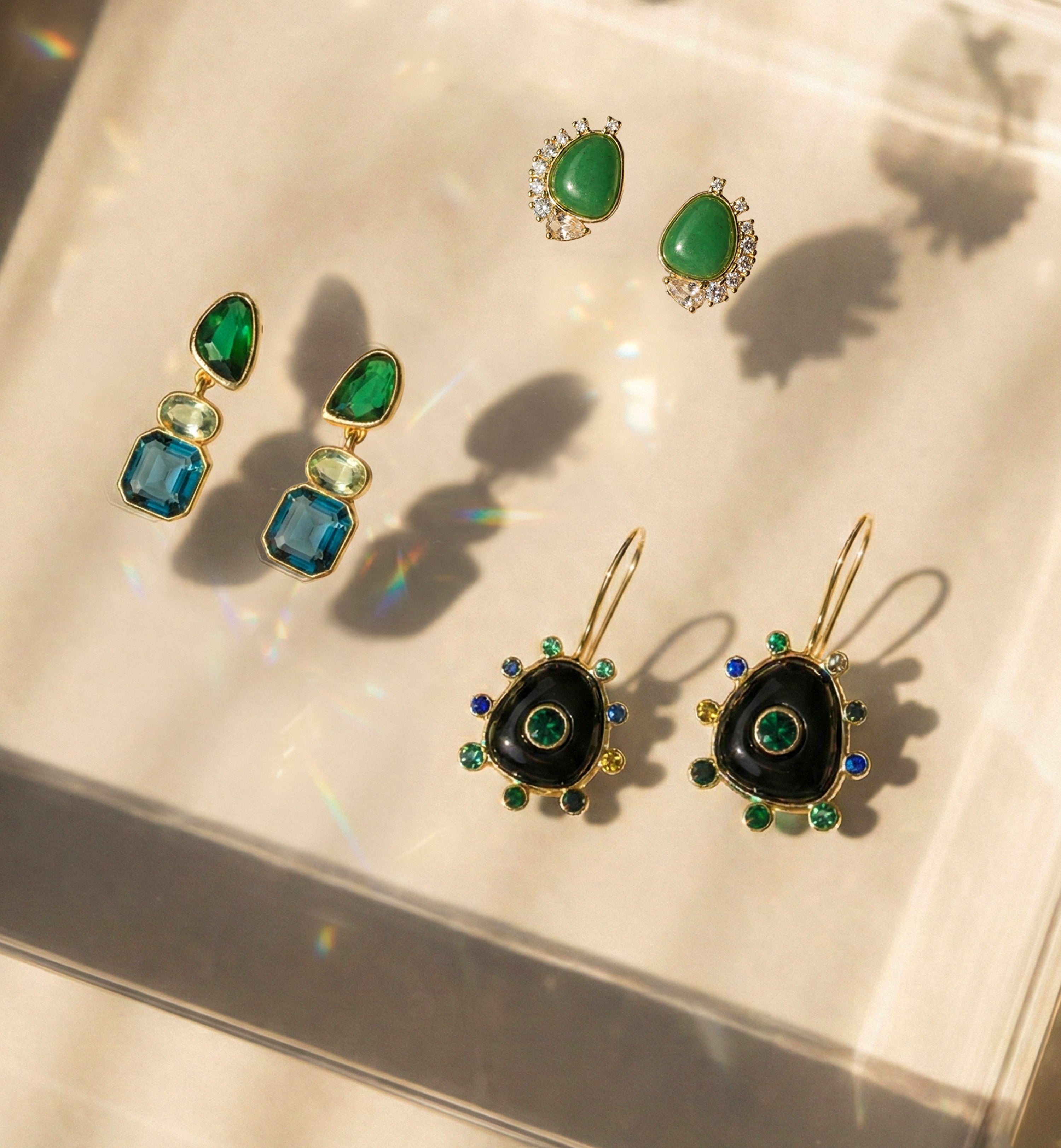 Three sets of statement earrings on a glass reflective background