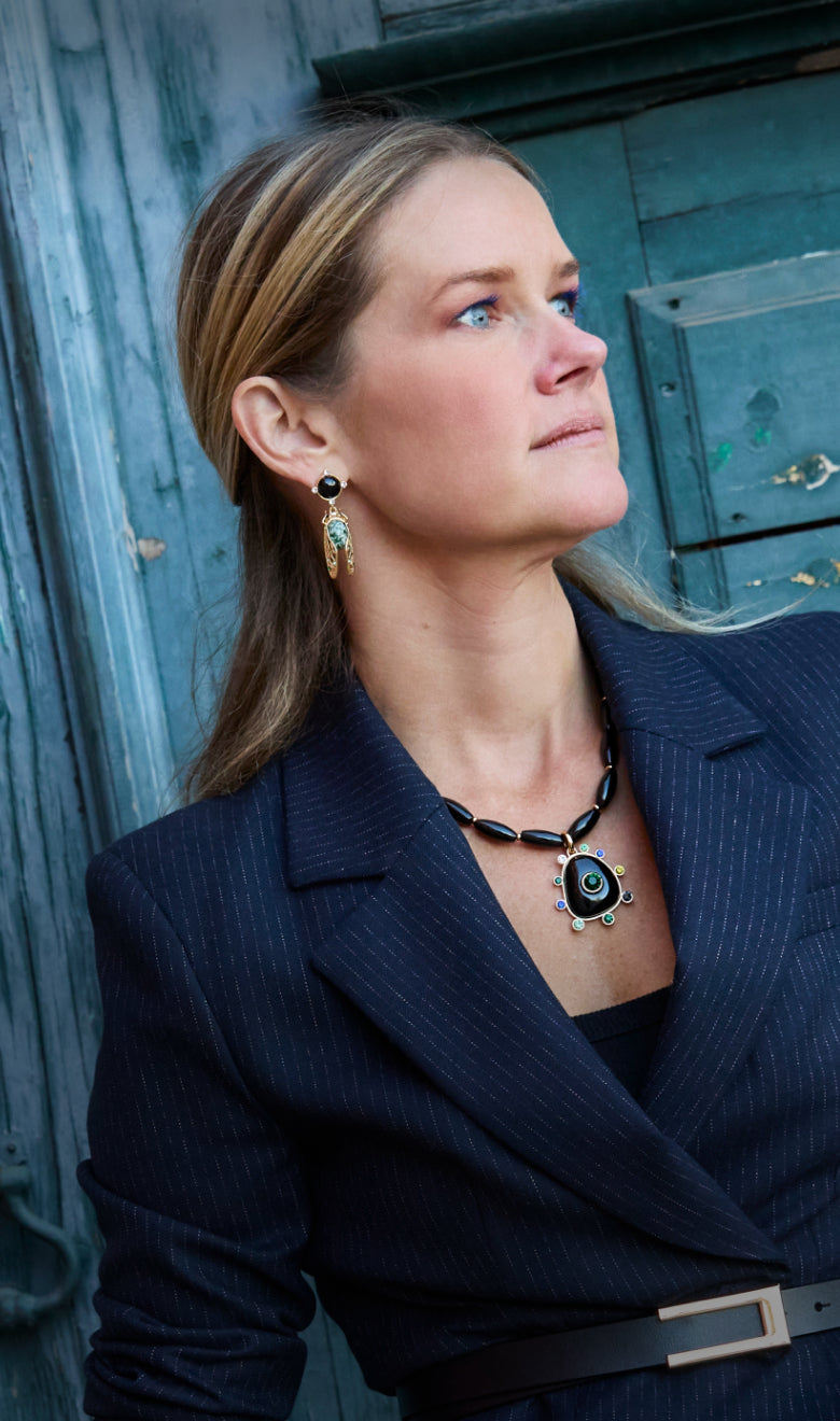 Model wearing statement earrings and necklace on a blue background