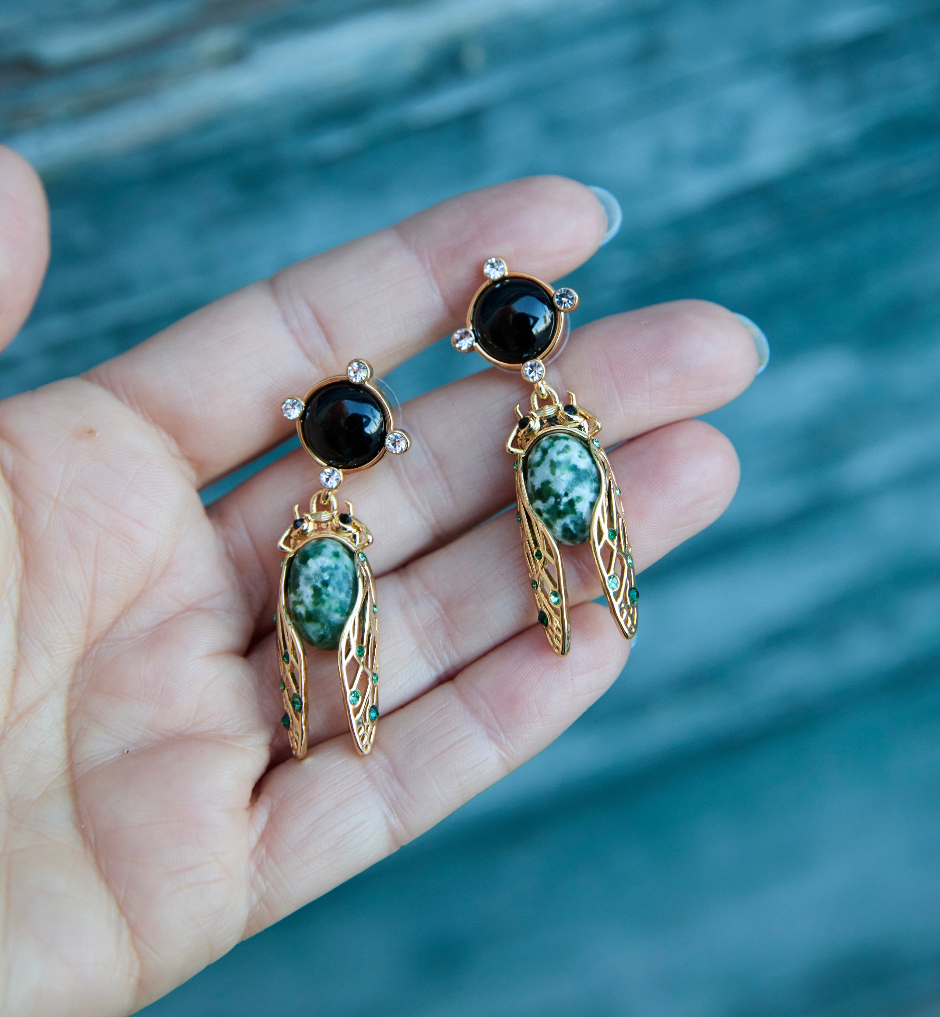 Cicada Inspired Earrings on a hand with a blue background
