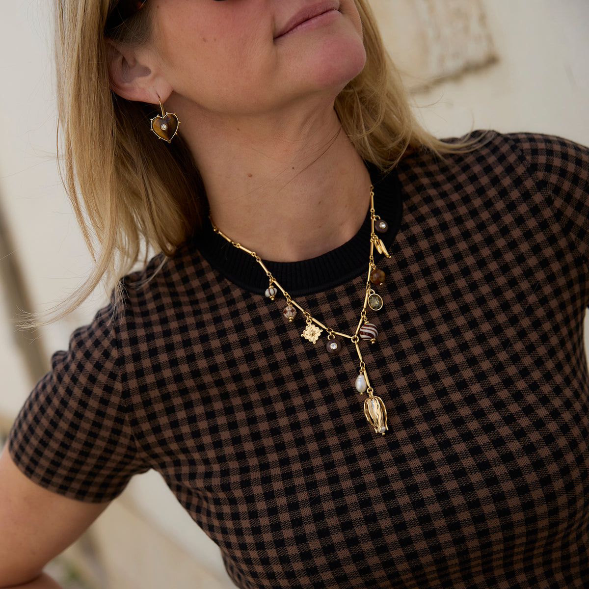 A close-up of a woman wearing gold heart-shaped dangle earrings and a gold pendant necklace.