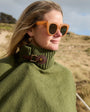 A close-up of a woman wearing gold heart-shaped dangle earrings on a grassy beach 