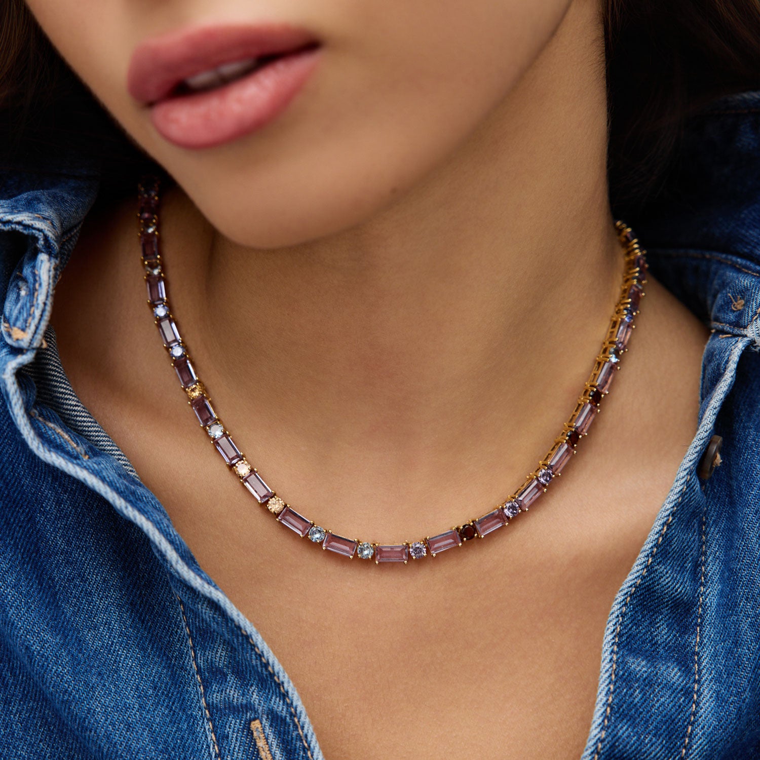 Necklace with purple crystals worn by a person wearing a denim jacket.