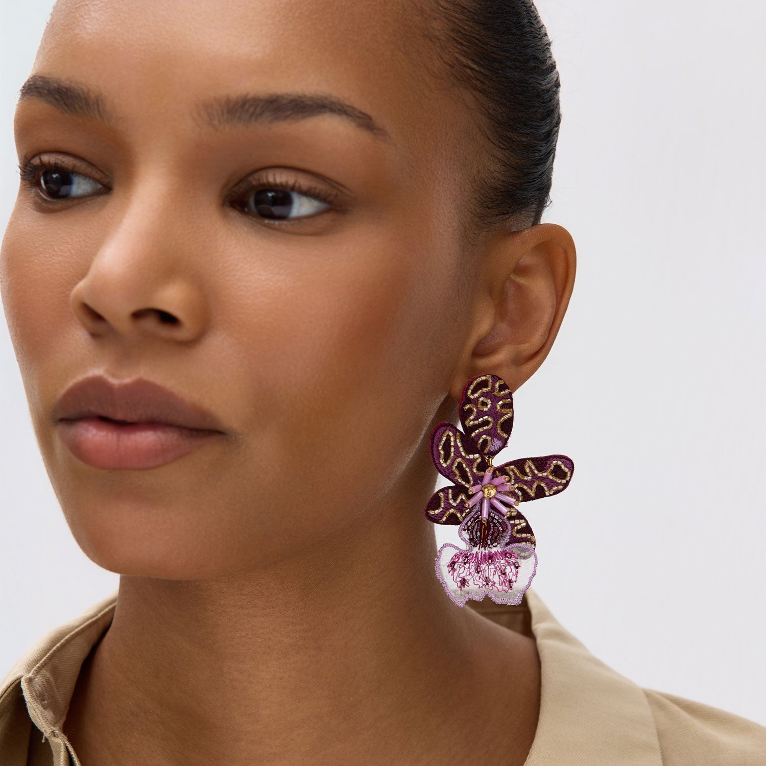Close-up of a woman wearing a pair of flower earrings against a neutral background