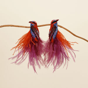 Red, Purple, and Blue Feather, Bead, and Thread Embroidered Bird Stud Earrings Staged on Branch on Tan Background