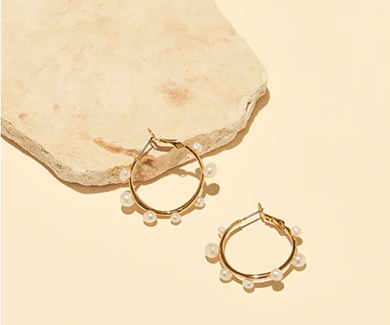 Gold hoop earrings with pearls on a beige stone surface