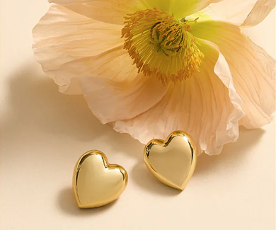 Gold heart-shaped earrings on a light pink flower background