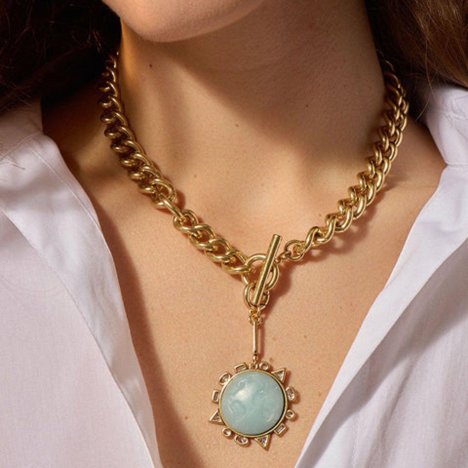 Gold chain necklace with a green pendant worn by a person in a white shirt.