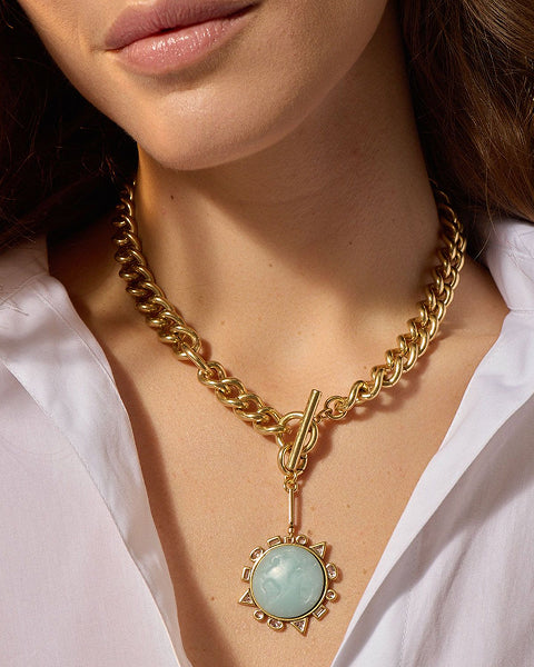 Gold chain necklace with a green pendant worn by a person in a white shirt.