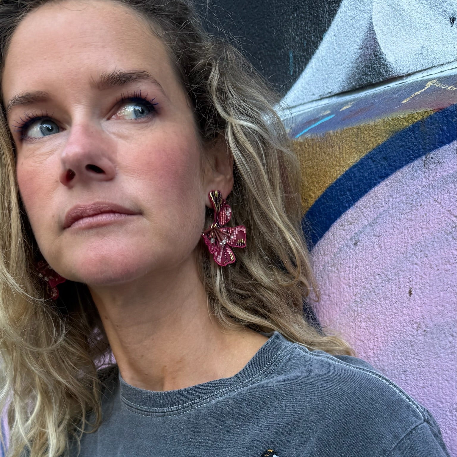Maggie wearing a graphic t-shirt with colorful designs and red earrings against a graffiti wall.