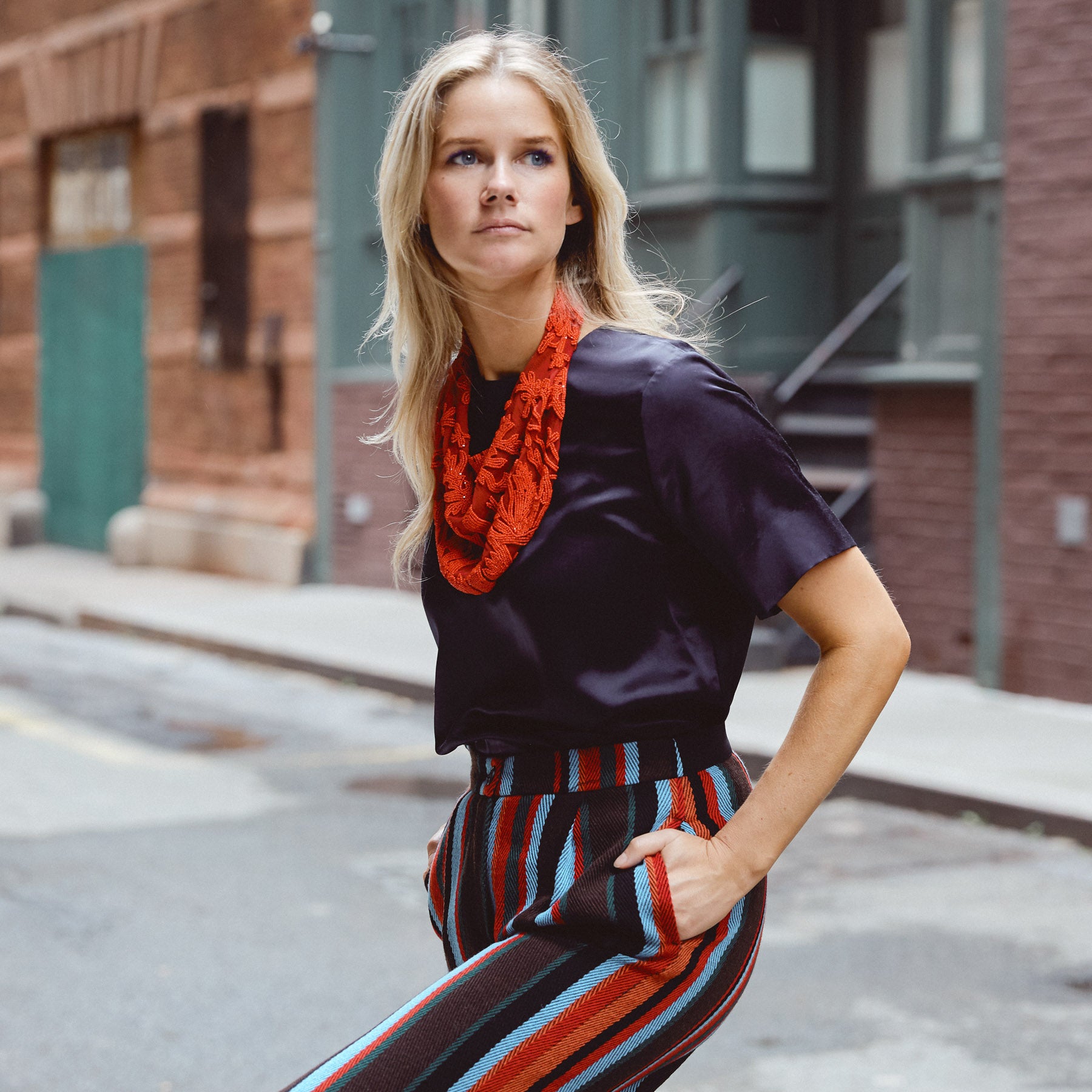 Maggie wearing navy top, striped pants, and red beaded scarf necklace in urban setting