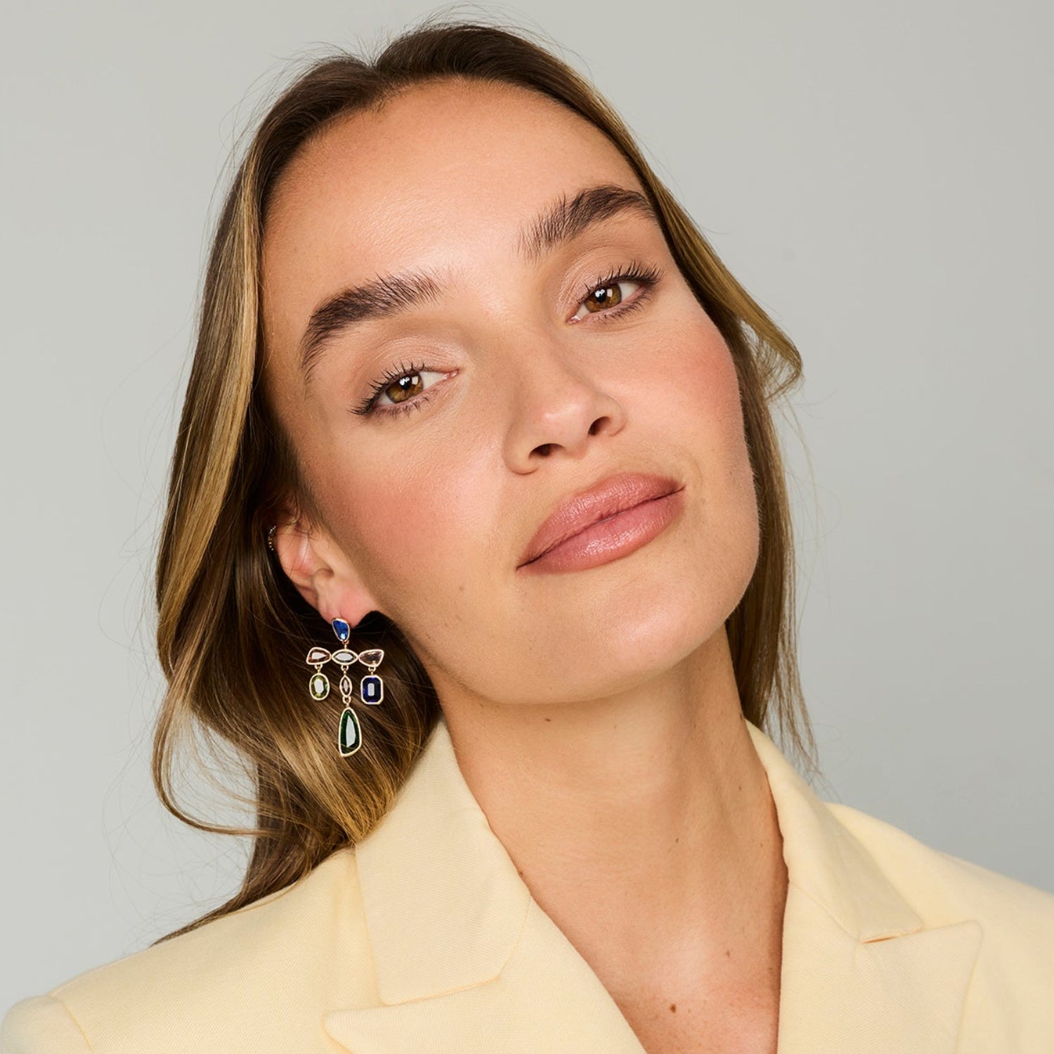 Colorful gold-tone statement earrings featuring blue, green, and clear faceted stones in a playful geometric design on model