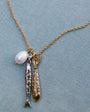 Necklace with fish charms and a pearl on a light blue fabric background