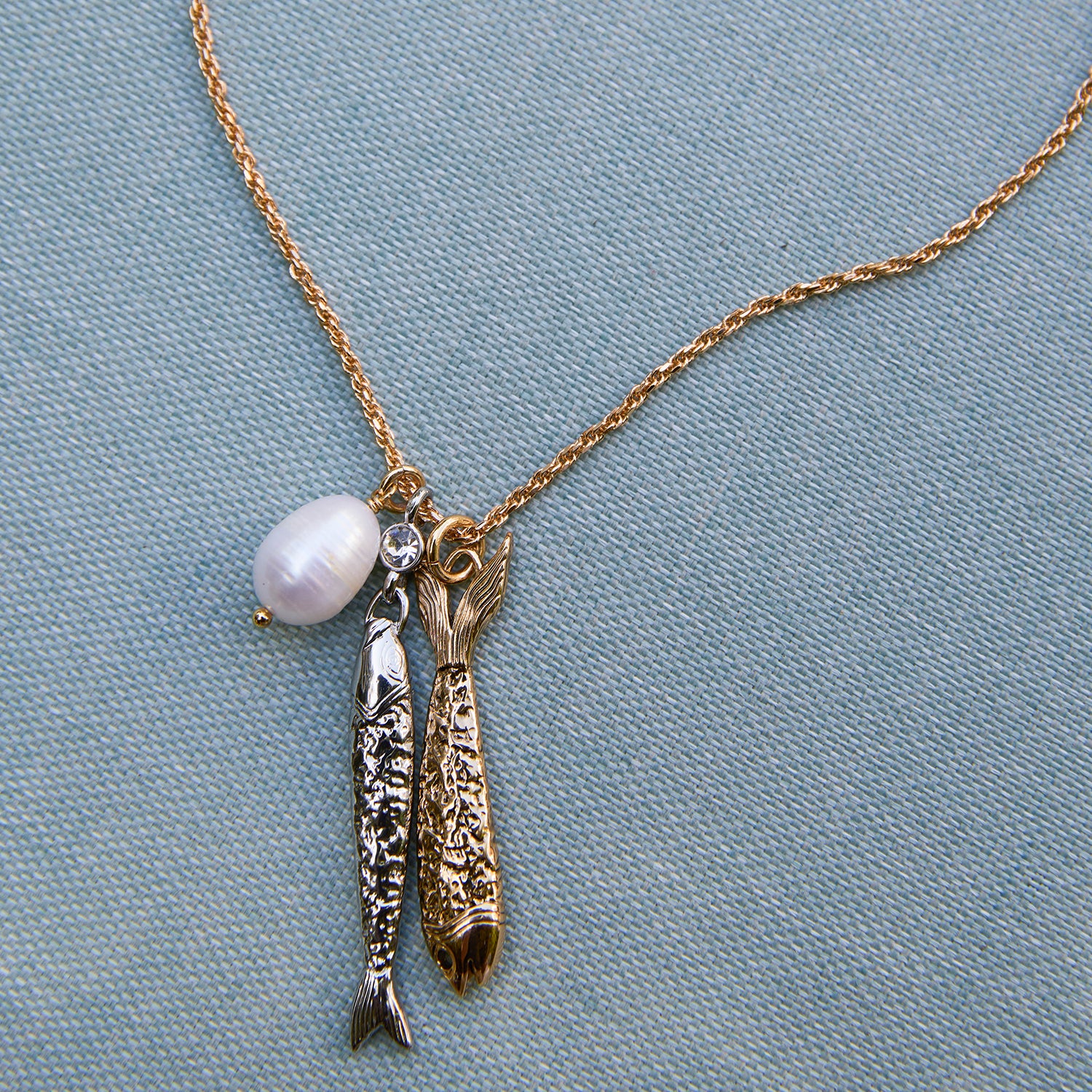 Necklace with fish charms and a pearl on a light blue fabric background