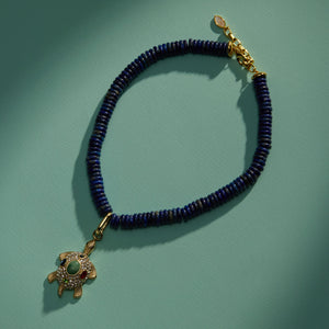 Crystal and Stone Turtle Charm on Blue Bead Strand Necklace Staged on Green Surface