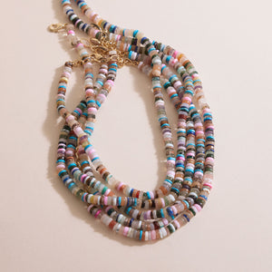Assortment of multi-colored beaded strand necklace styled on cream surface