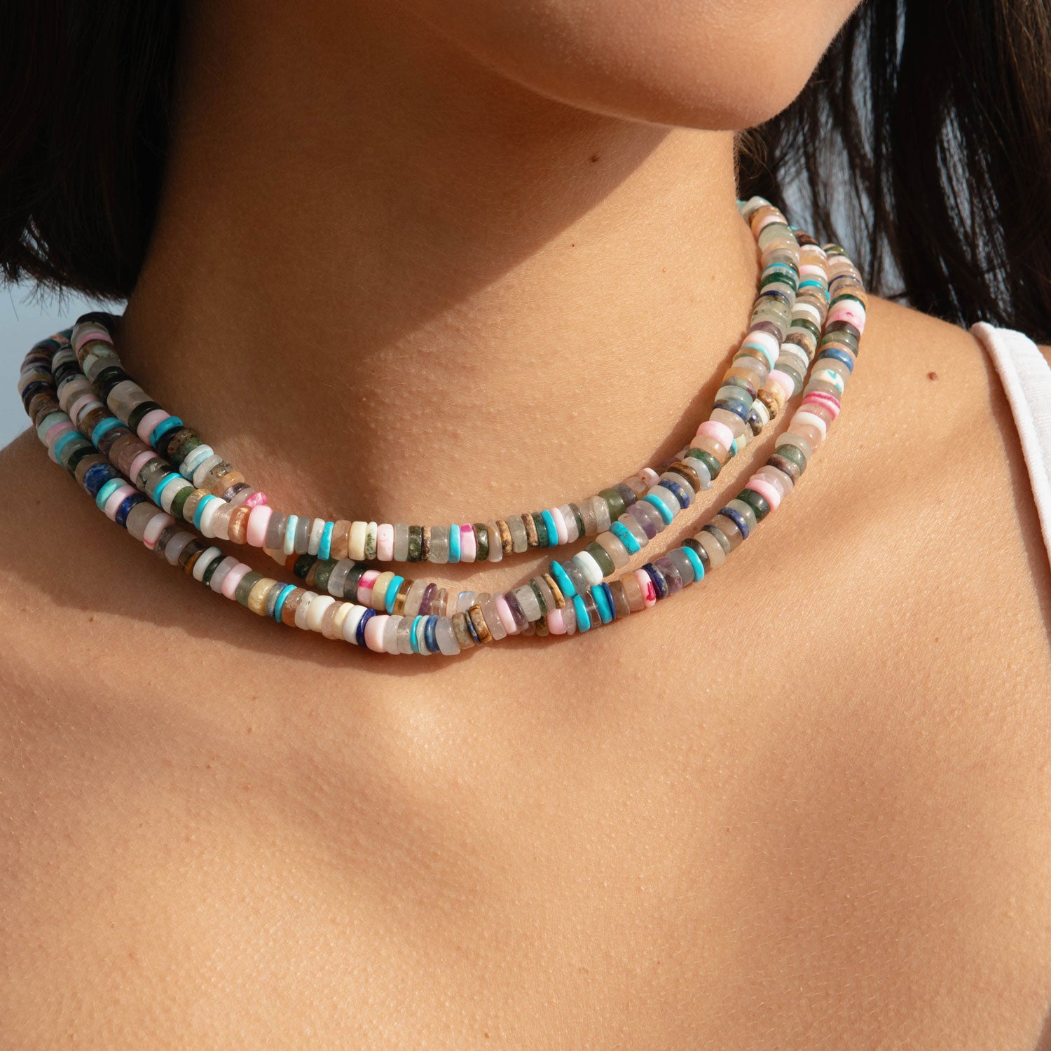 Multi-colored beaded strand necklace styled in a stack on model's neck