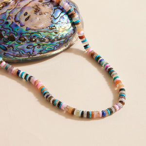 Multi-colored beaded strand necklace styled with shell on cream surface