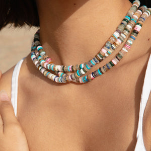Multi-colored beaded strand necklace styled in a stack on model's neck