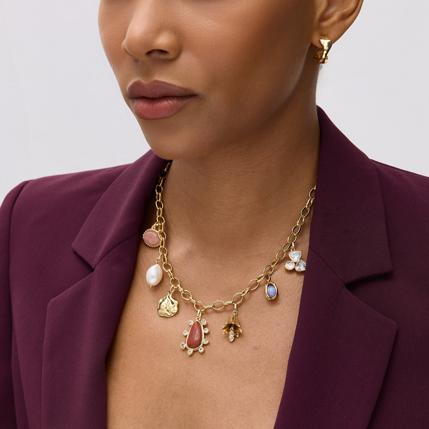 Woman wearing a gold necklace with various charms against a neutral background